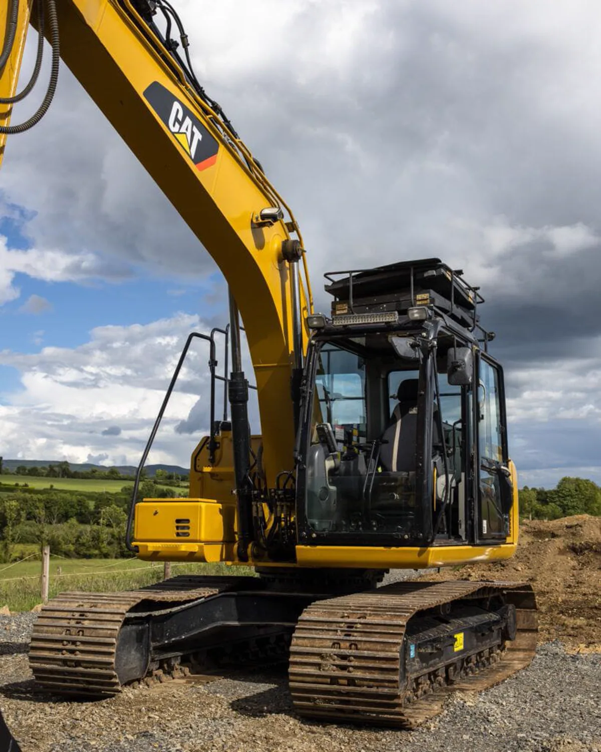 CAT tracked excavator parked on gravel with Irish countryside behind