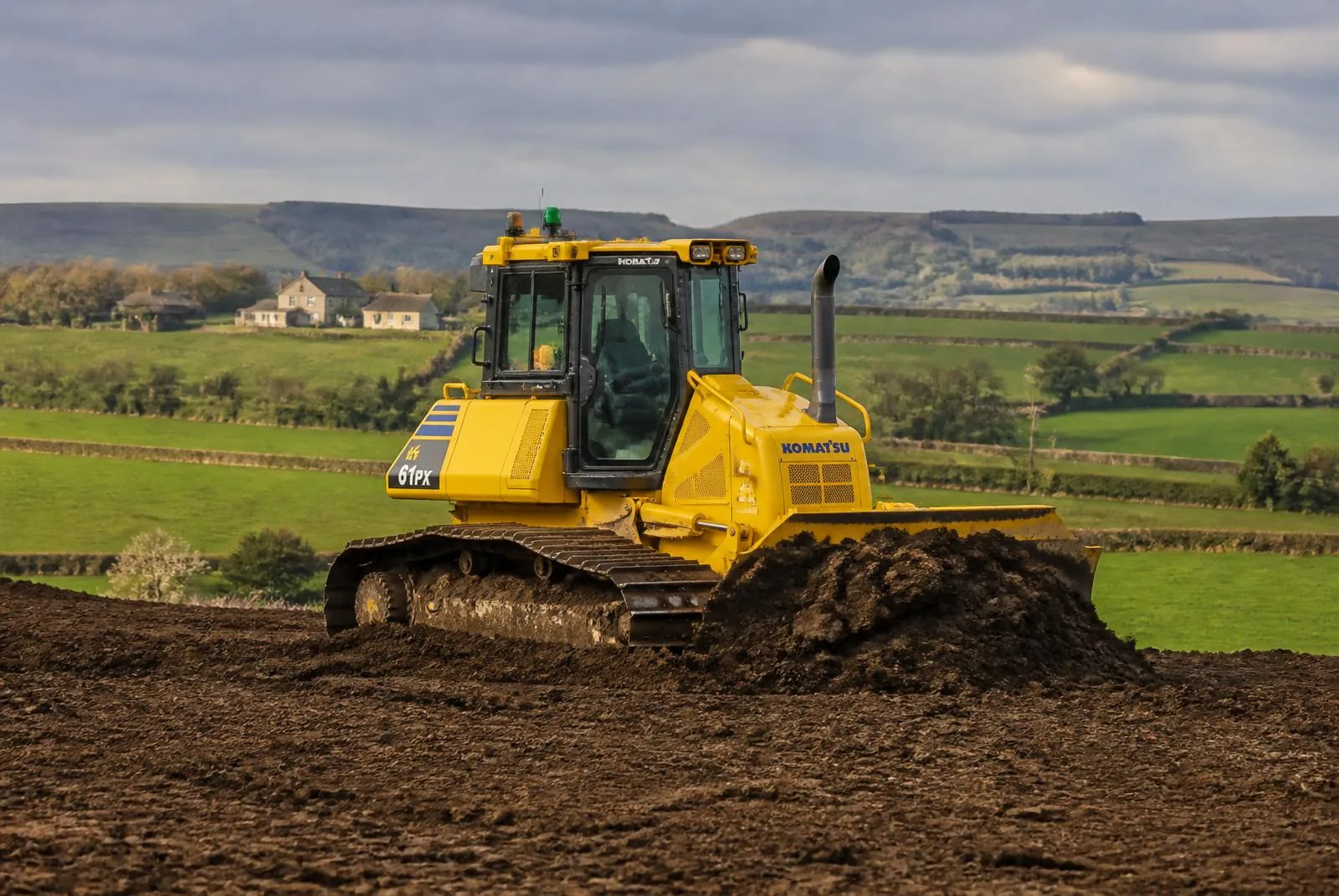 Tracked bulldozer levelling ground on a rural site with green Irish fields and hedgerows behind