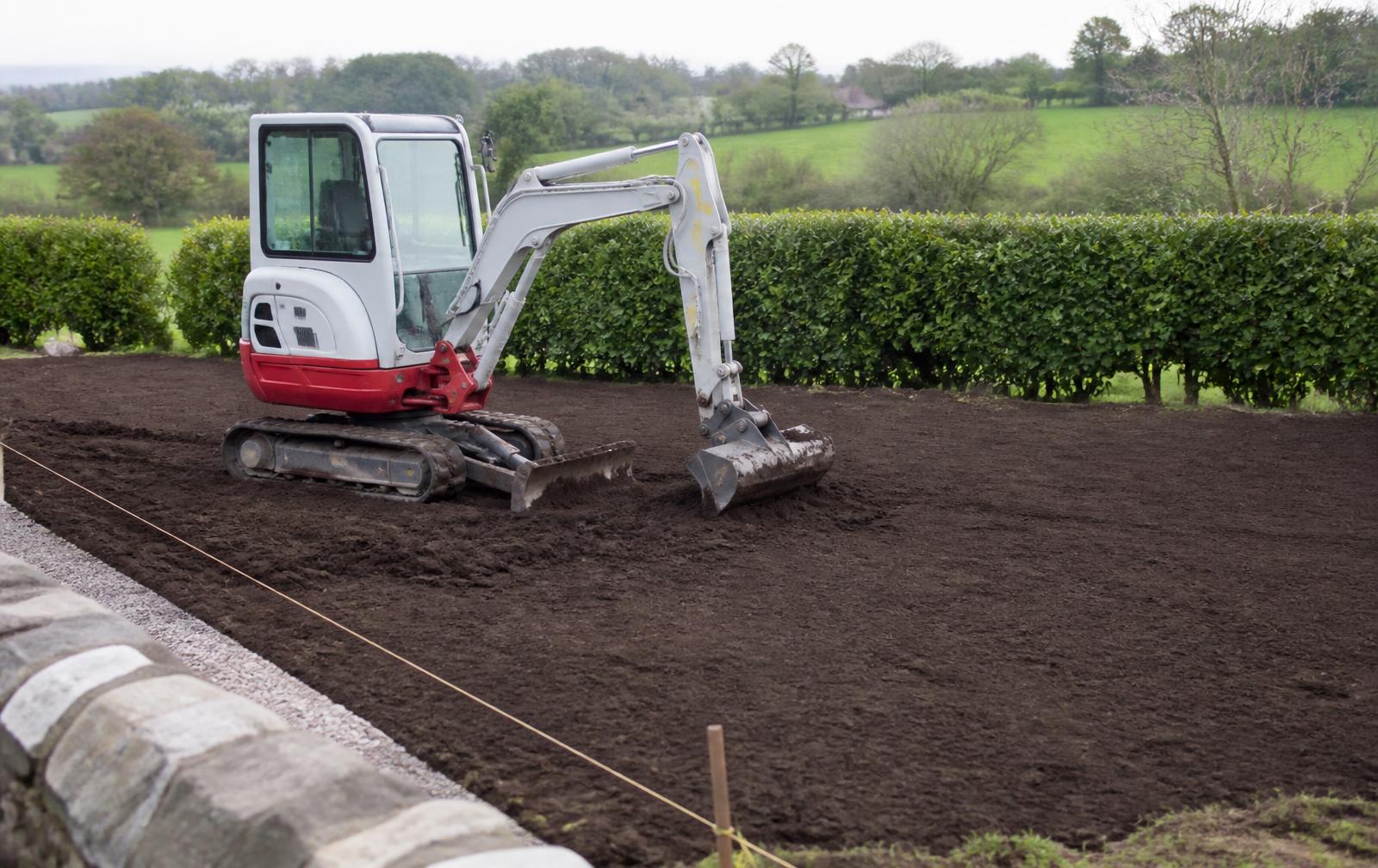 Compact tracked digger spreading fresh topsoil to shape a new garden lawn