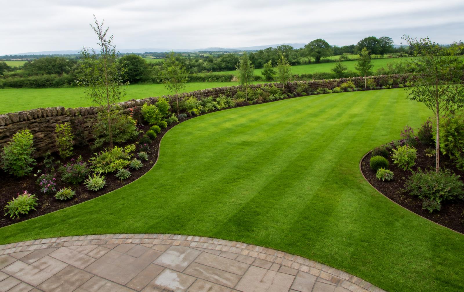 Freshly finished striped lawn with curved planted borders and a stone wall in the Irish countryside